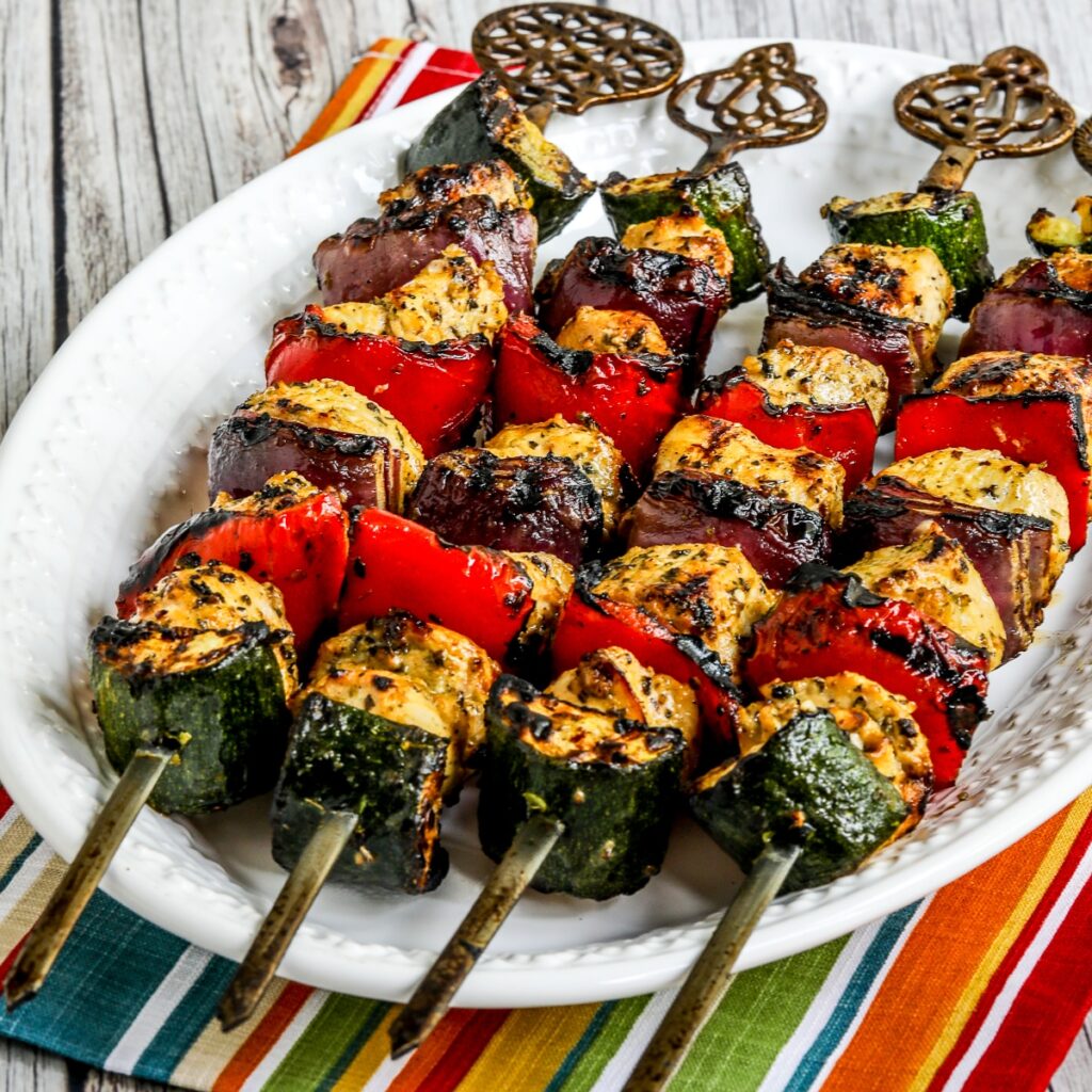 Square image of Grilled Chicken Kabobs with Vegetables on platter with striped napkin.