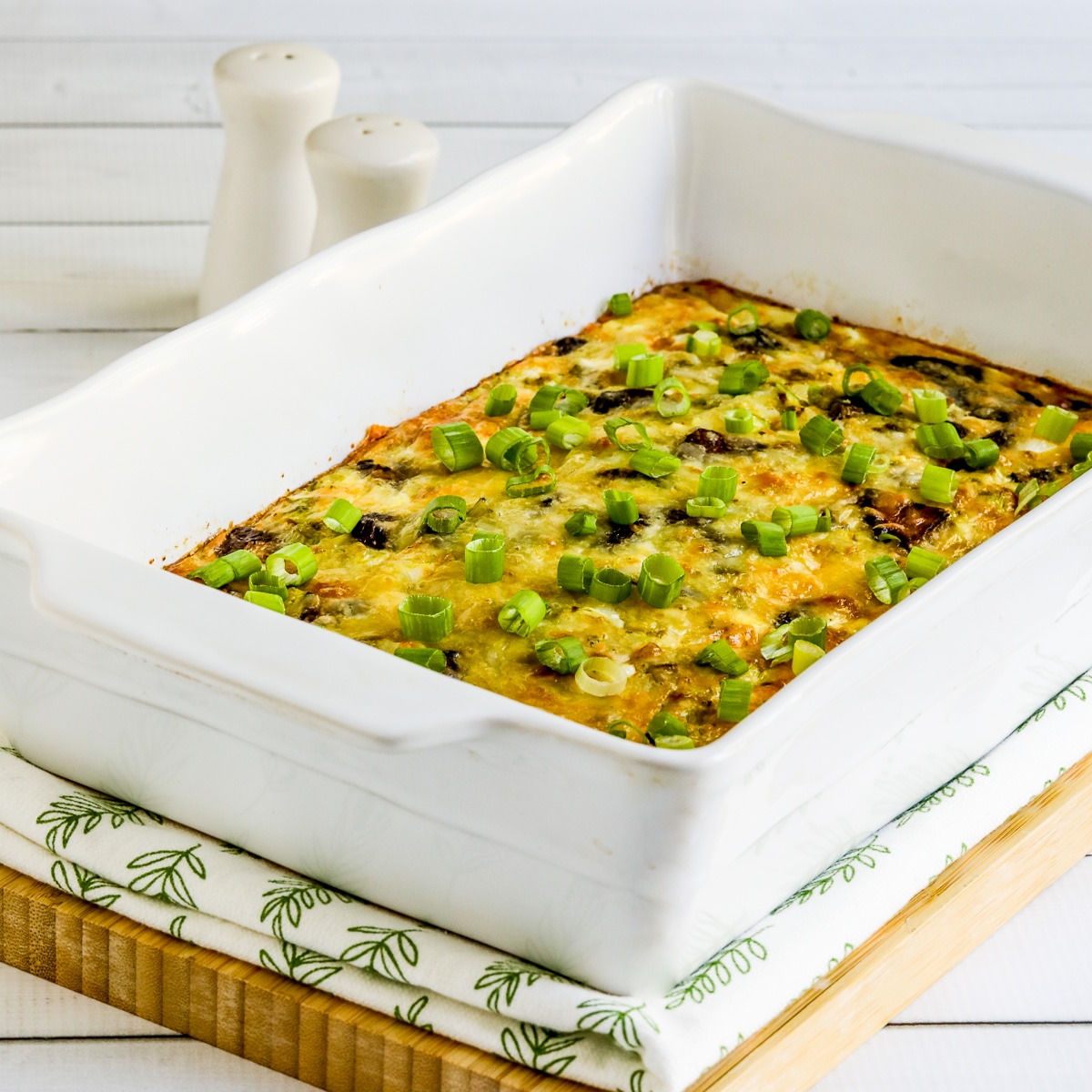 Square image for Cheesy Vegetarian Breakfast Casserole shown in baking dish on napkin and cutting board.